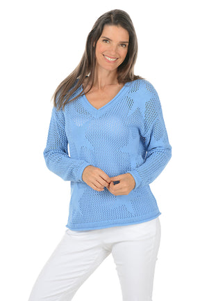 Woman wearing a light blue sweater and white pants on a white background.