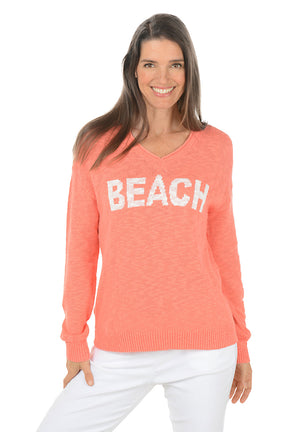 Woman wearing a coral sweater with 'BEACH' text on a white background.