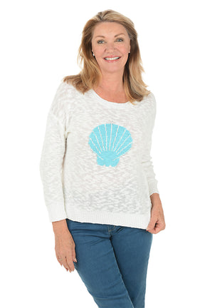 Woman wearing a white sweater with a blue shell design on a white background.