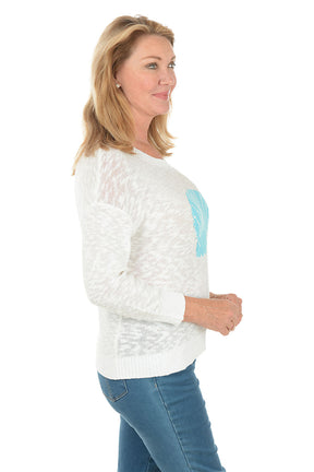 Woman wearing a white sweater with a blue shell design on a white background. Side shot.