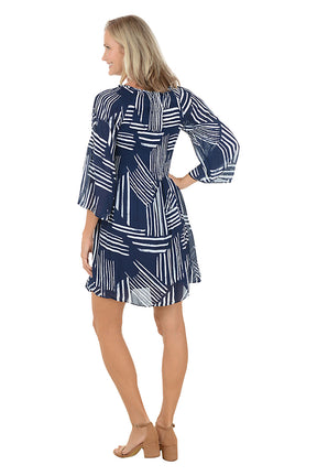 Woman wearing a navy blue and white "sketched lines" patterned dress with 3/4 bell sleeves. Back shot.