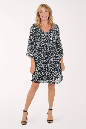 A woman wearing a black and white 3/4 sleeve dress with a heart pattern.