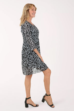 A woman wearing a black and white 3/4 sleeve dress with a heart pattern.