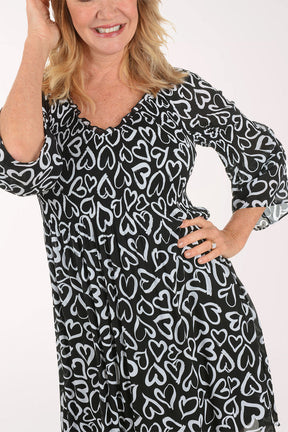 A woman wearing a black and white 3/4 sleeve dress with a heart pattern.