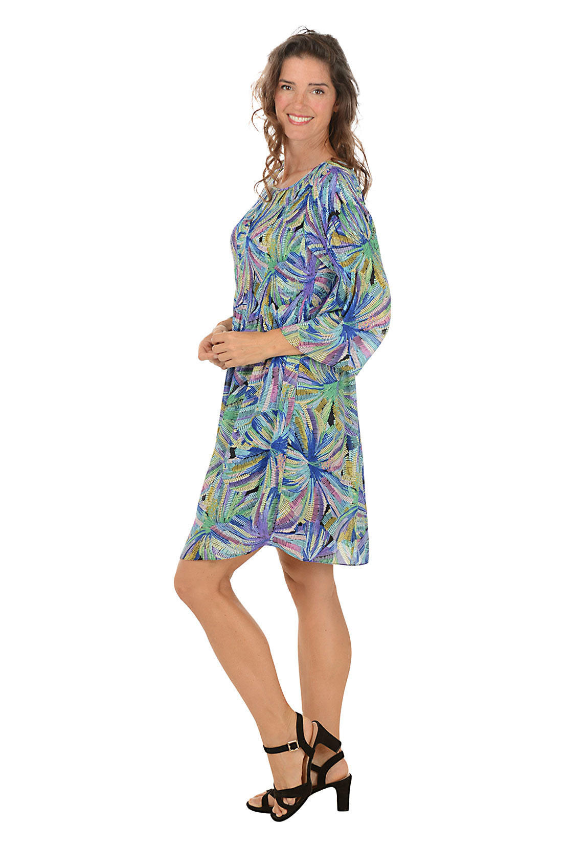 Woman wearing a colorful floral dress on a white background. Side shot.