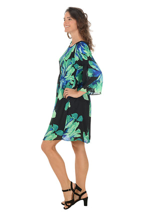 Woman wearing a black dress with blue and green floral pattern on a white background. Side shot.