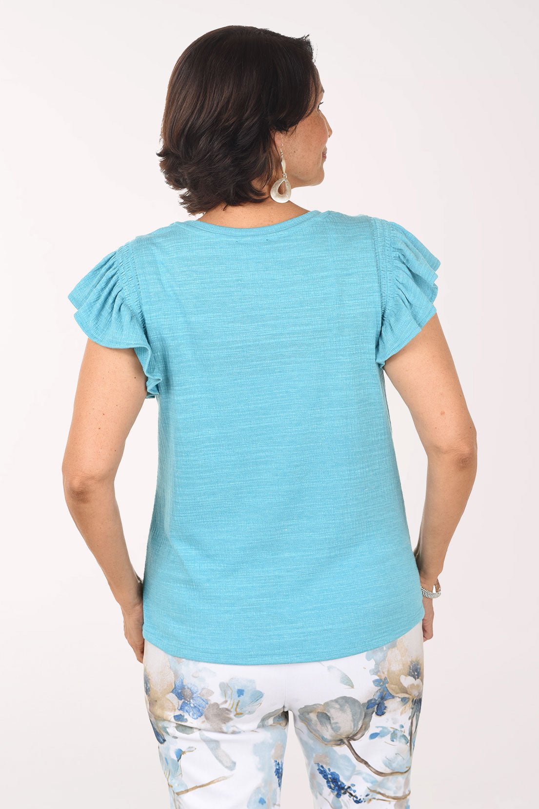 Woman wearing a light blue ruffled blouse with floral pants on a white background