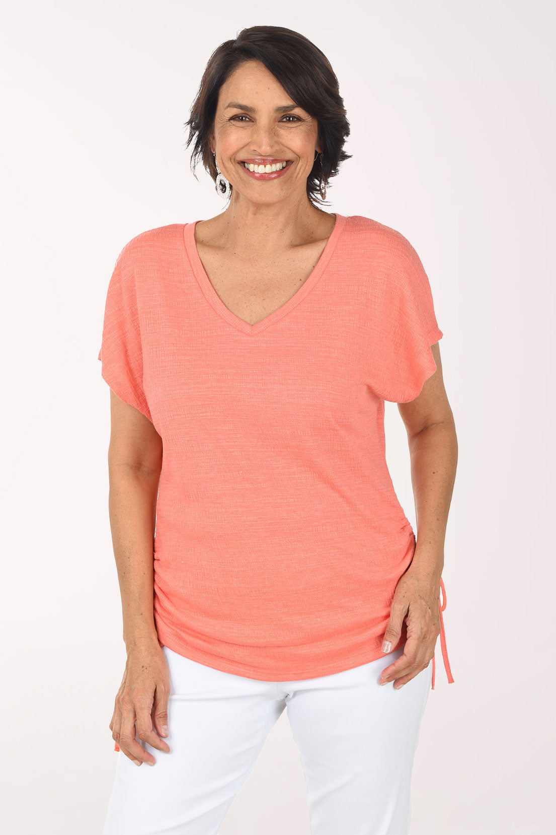 Woman wearing a coral t-shirt and white pants on a white background