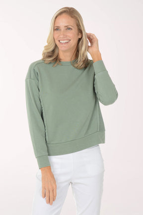 Woman wearing a green sweater and white pants on a light pink background
