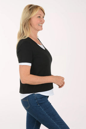 Woman wearing a black t-shirt with white trim and blue jeans on a white background