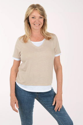 Woman wearing a beige t-shirt over a white shirt with blue jeans on a white background