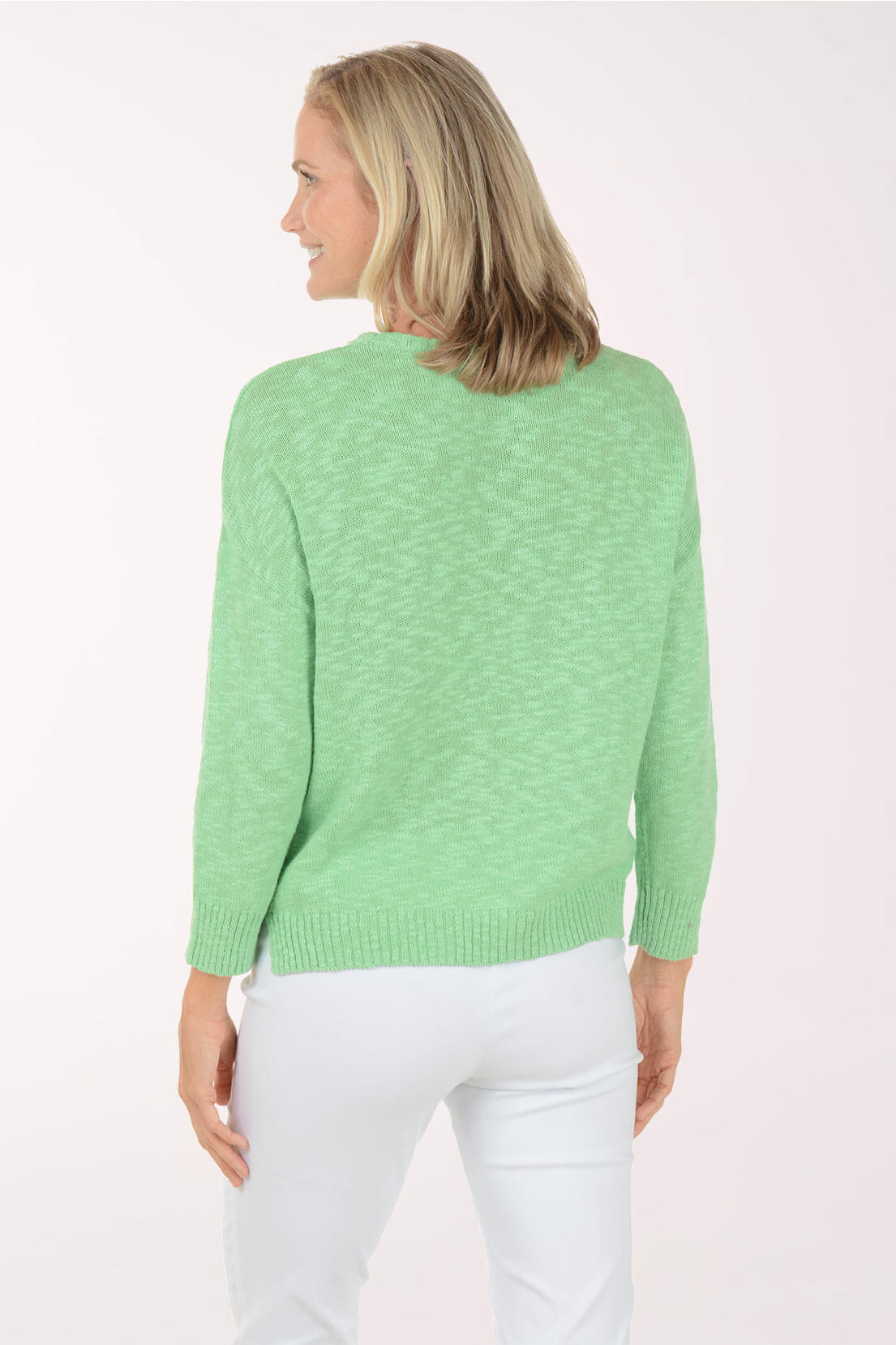 A woman shown from the back wearing a light green knit sweater and white pants against a plain light background.