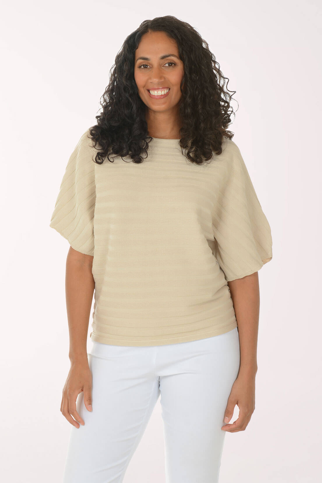 Woman wearing a beige sweater and white pants on a white background