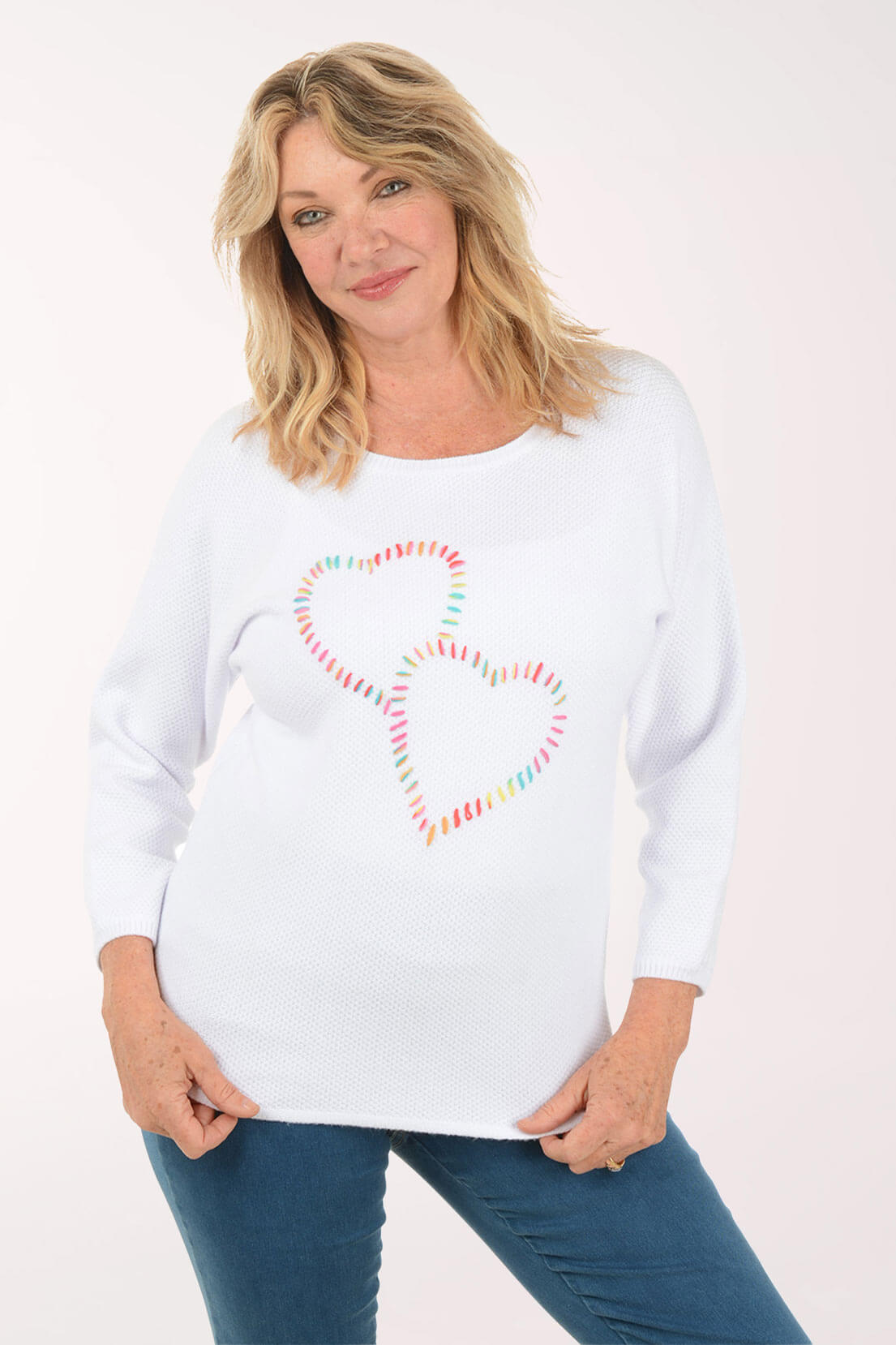 Woman wearing a white sweatshirt with a colorful heart design on a plain background