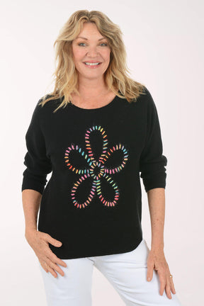 Woman wearing a black sweater with a colorful flower design on a white background