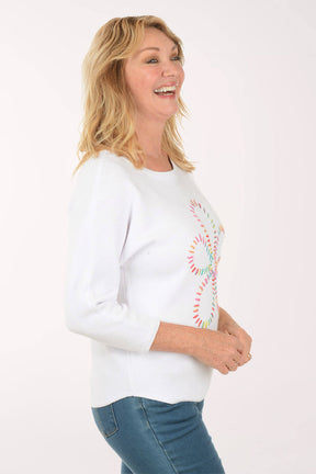 Woman wearing a white sweatshirt with a colorful daisy design on a white background. Side shot