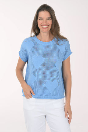 Woman wearing a light blue knit top with heart patterns on a white background