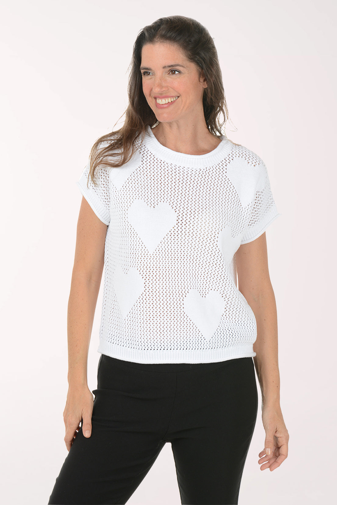 Woman wearing a white knit top with heart patterns on a plain background