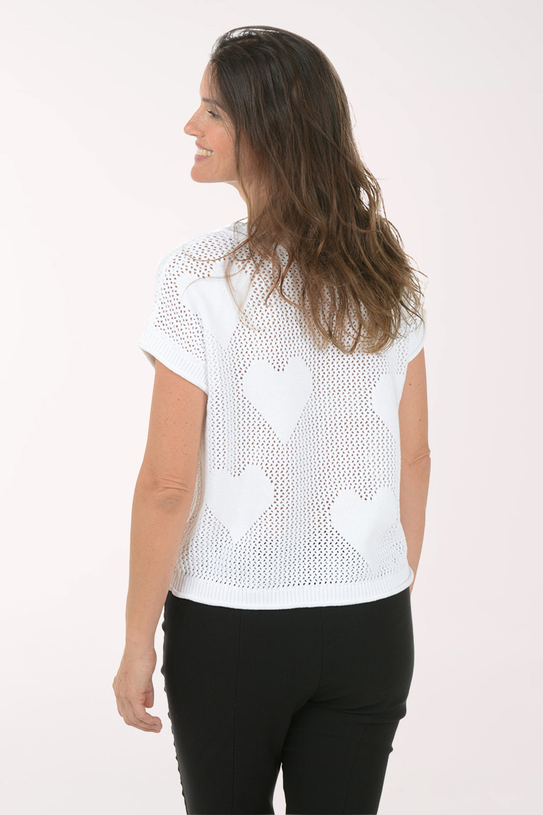 Woman wearing a white knit top with heart patterns on a plain background