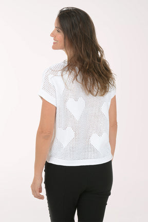 Woman wearing a white knit top with heart patterns on a plain background