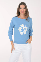 Woman wearing a light blue sweater with a white floral design on a white background