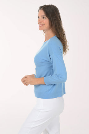Woman wearing a light blue sweater with a white floral design on a white background