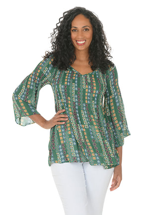 Woman wearing a patterned green blouse with white pants on a white background.