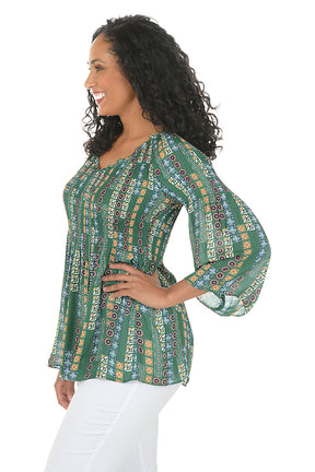 Woman wearing a patterned green blouse with white pants on a white background. Side shot.