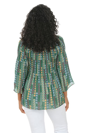 Woman wearing a patterned green blouse with white pants on a white background. Back shot.