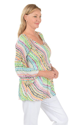 Woman wearing a colorful patterned top on a white background. Side shot.