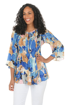 Woman wearing a colorful floral blouse with white pants on a white background. Second front shot.