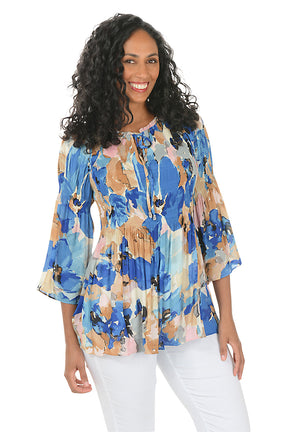 Woman wearing a colorful floral blouse with white pants on a white background.