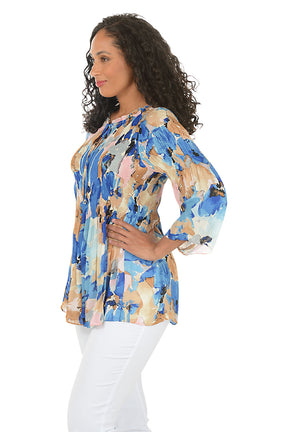 Woman wearing a colorful floral blouse with white pants on a white background. Side shot.