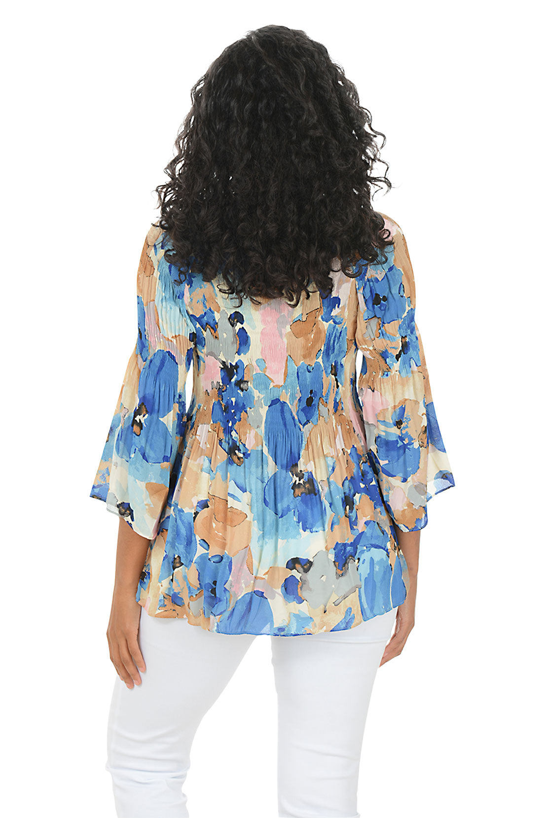 Woman wearing a colorful floral blouse with white pants on a white background. Back shot.