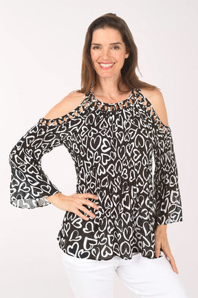 Woman wearing a black and white heart patterned blouse with cold shoulder design on a white background