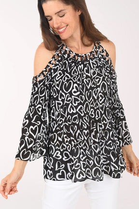 Woman wearing a black and white heart patterned blouse with cold shoulder design on a white background