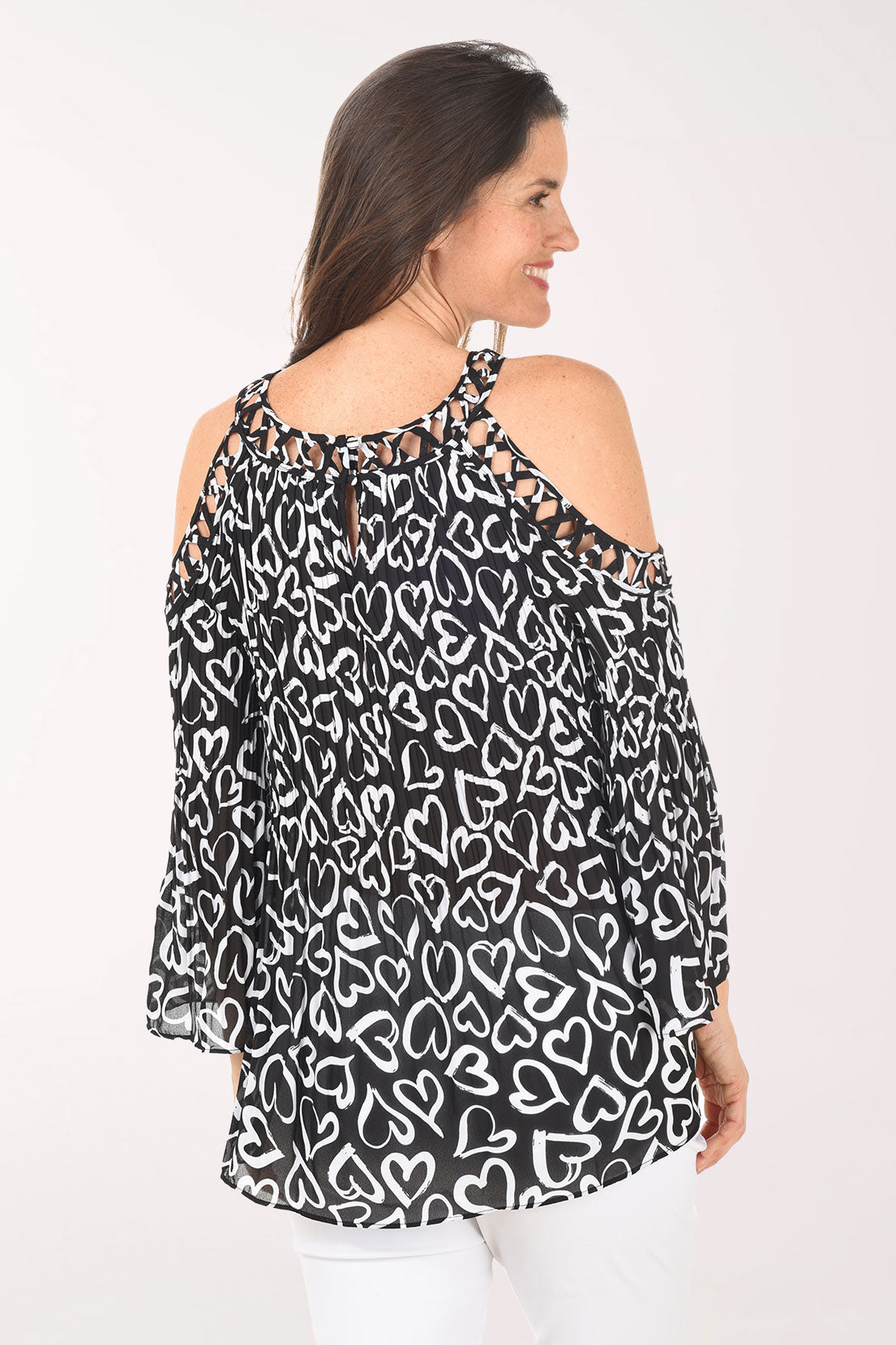 Woman wearing a black and white heart patterned blouse with cold shoulder design on a white background