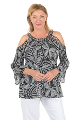 Woman wearing a black and white patterned blouse with cold shoulder design on a white background.
