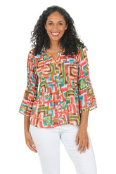 Woman wearing a colorful patterned blouse with white pants on a white background.