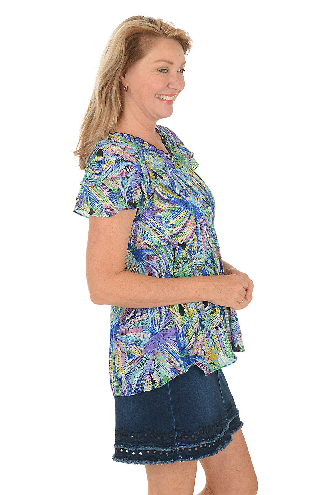 Woman wearing a colorful floral blouse with a white background. Side shot.