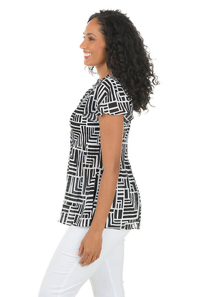 Woman wearing a black and white geometric patterned blouse with white pants on a white background. Side shot.