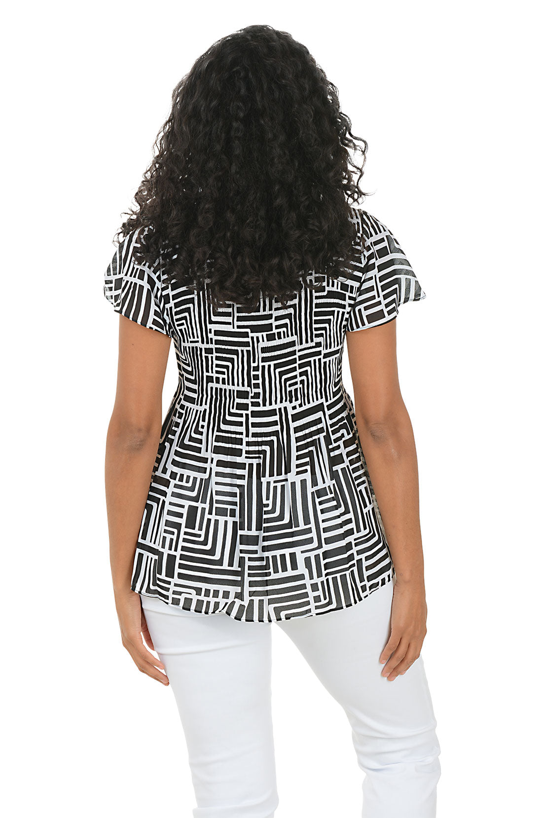 Woman wearing a black and white geometric patterned blouse with white pants on a white background. Back shot.