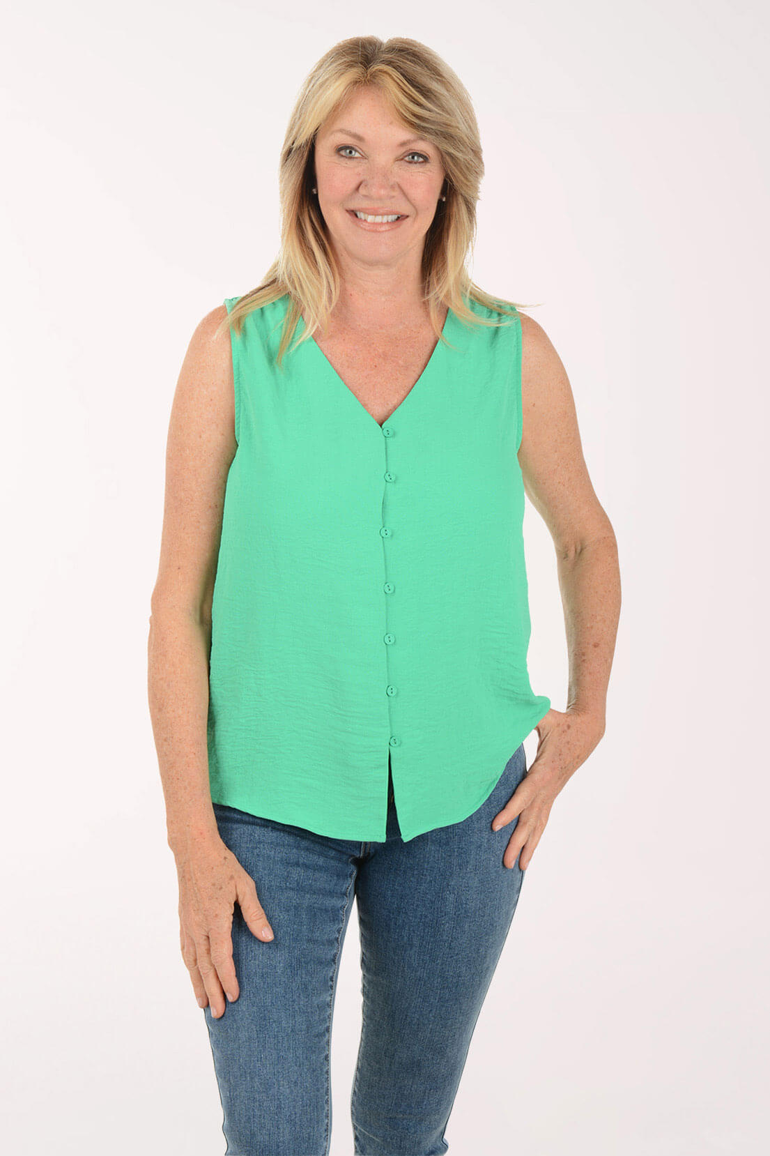 Woman wearing a green sleeveless blouse and blue jeans on a white background
