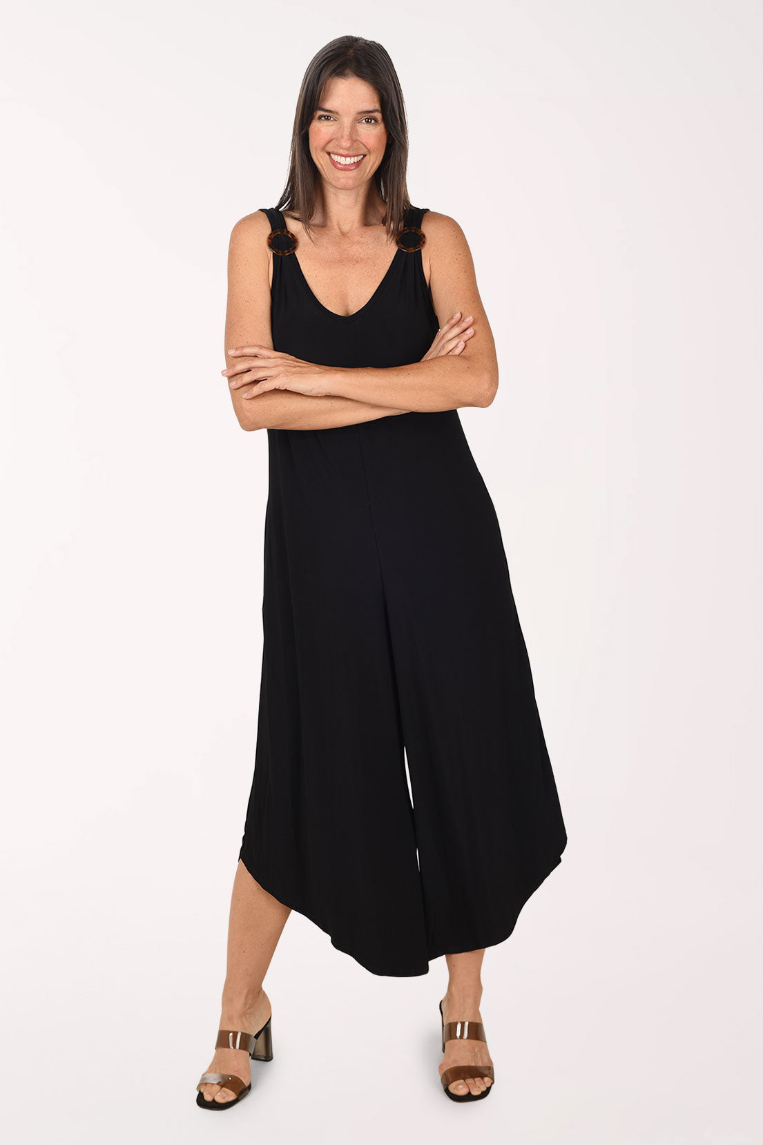 Front view of a model wearing the Sami and Jo Ringed Strap Sleeveless Jumpsuit in black, with tortoiseshell rings on the shoulder straps, a V-neckline and wide cropped legs, worn with brown heeled sandals.