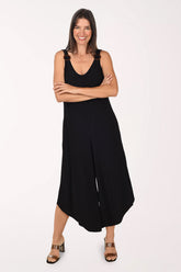 Front view of a model wearing the Sami and Jo Ringed Strap Sleeveless Jumpsuit in black, with tortoiseshell rings on the shoulder straps, a V-neckline and wide cropped legs, worn with brown heeled sandals.