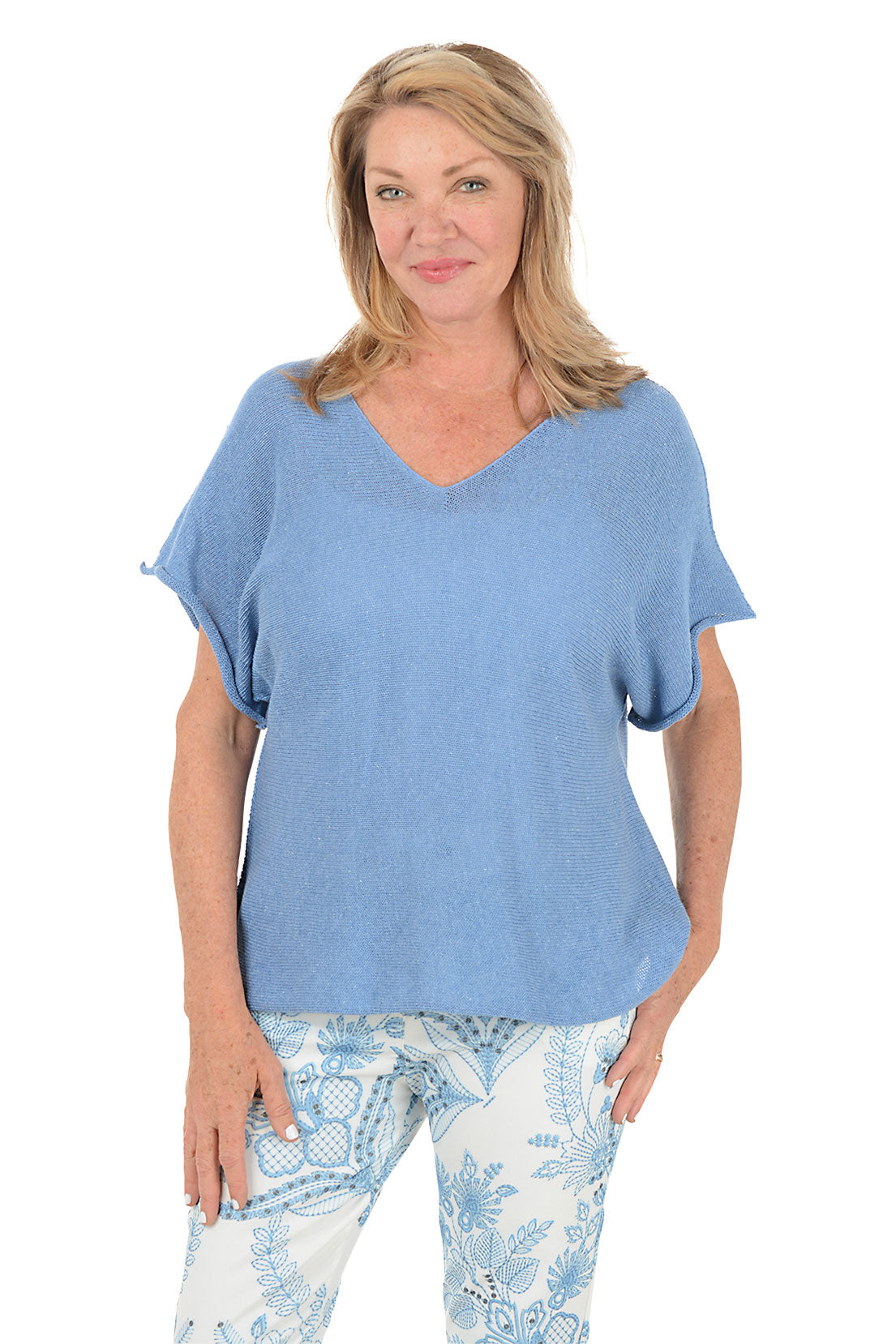 Woman wearing a blue top and patterned pants on a white background.