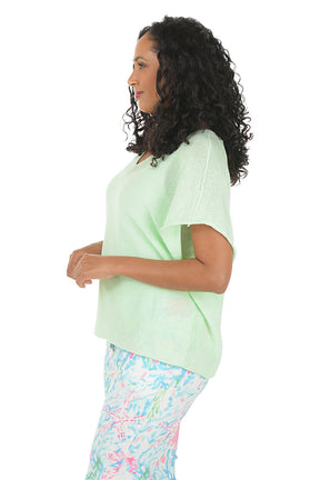 Woman wearing a light green top and colorful pants on a white background. Side shot.