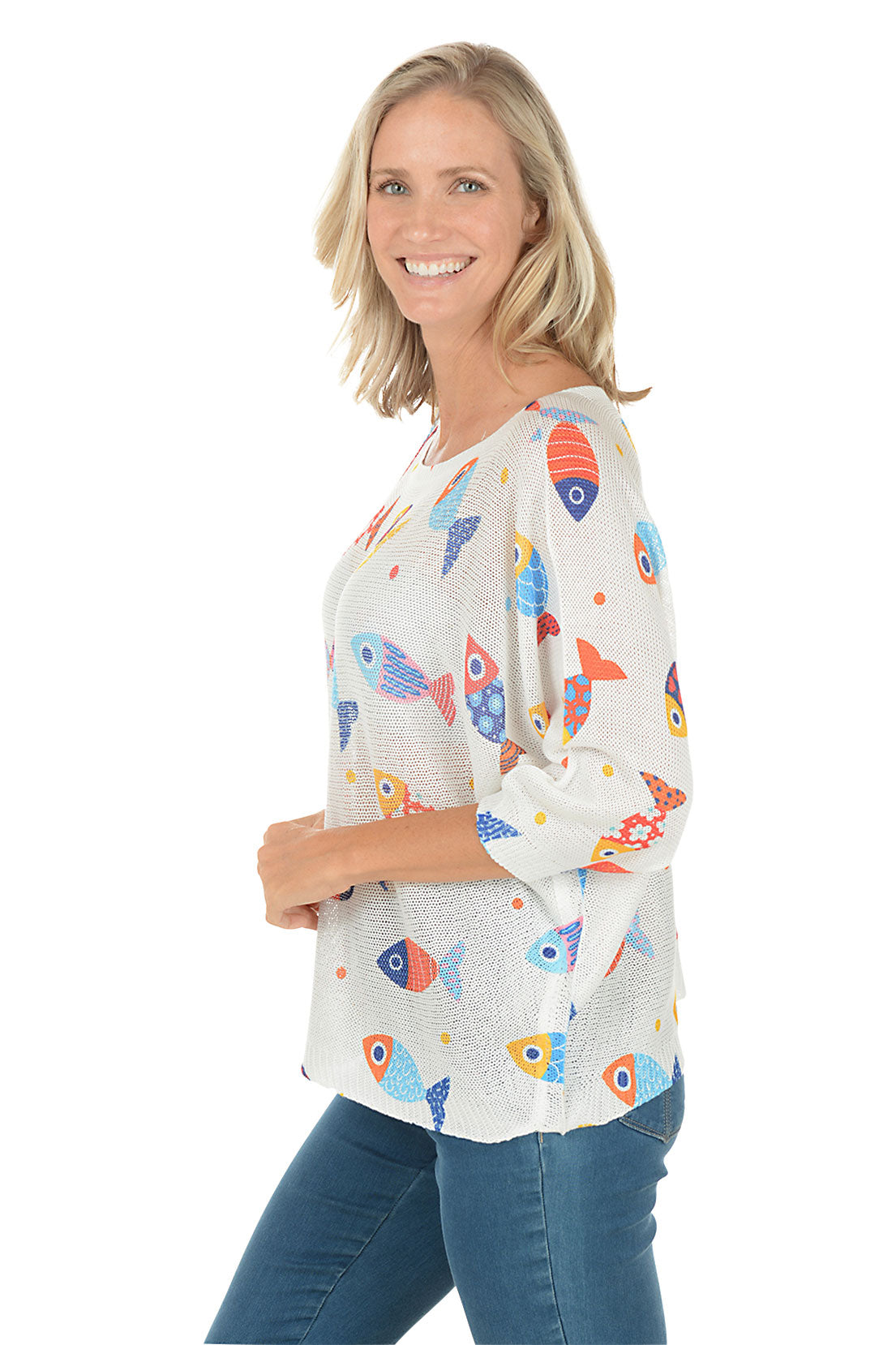Woman wearing a white sweater with colorful fish patterns on a white background. Side shot.