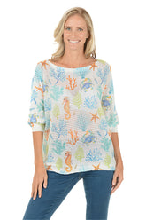 Woman wearing a colorful marine-themed shirt with seahorses and coral on a white background.