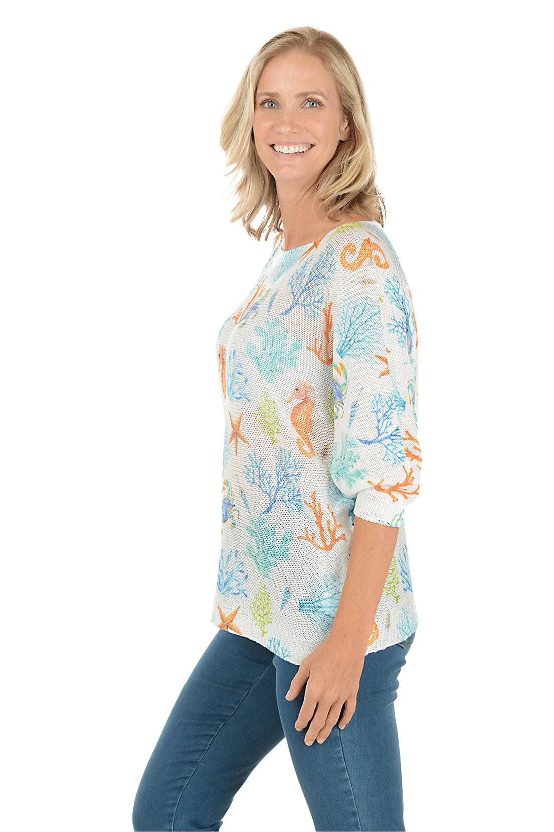 Woman wearing a colorful marine-themed shirt with seahorses and coral on a white background. Side shot.